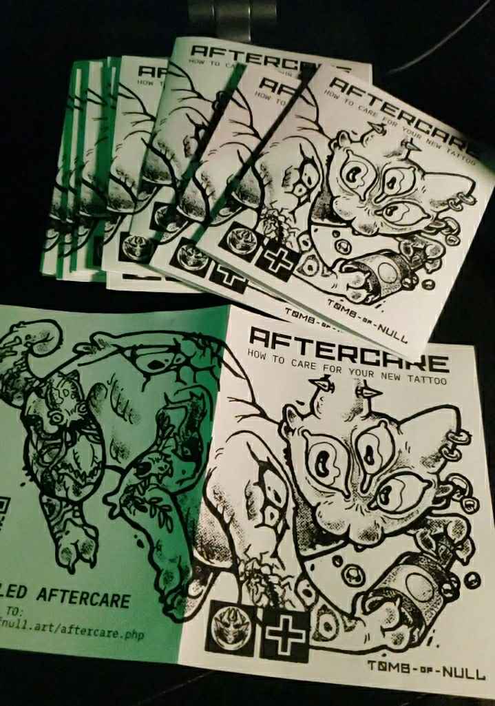 Photo of several pamphlets featuring the weird, tattooed cat creature. Text: Aftercare. How to care for your new tattoo. Tomb of Null.